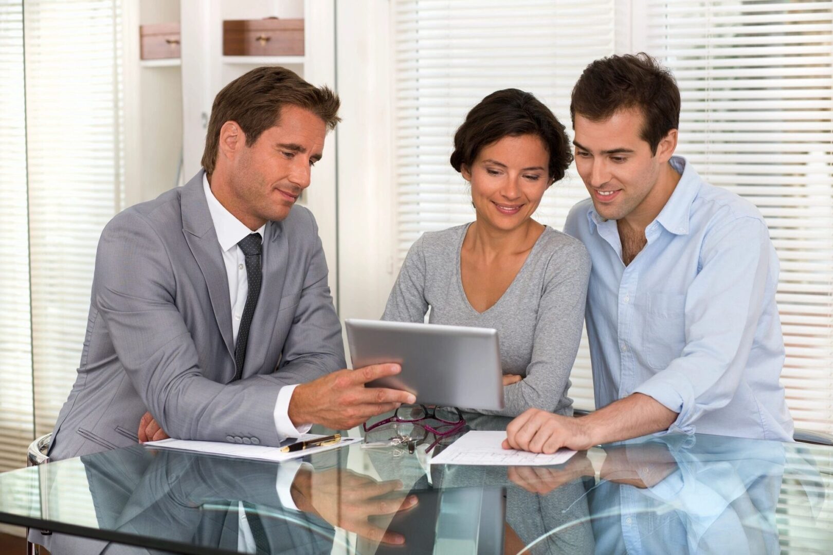 Three people sitting at a table looking at a tablet.